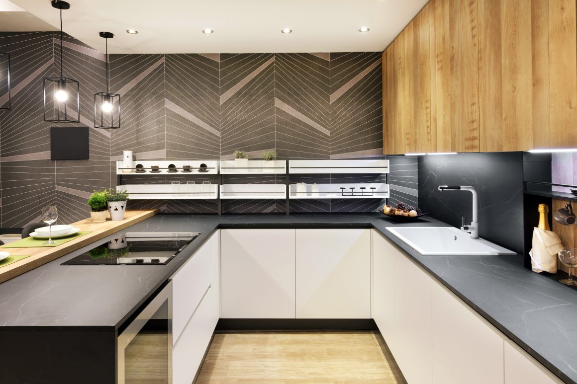 Cuisine moderne en U, avec plans noirs, armoires blanches, comptoir en bois, éclairage encastré et suspension design.