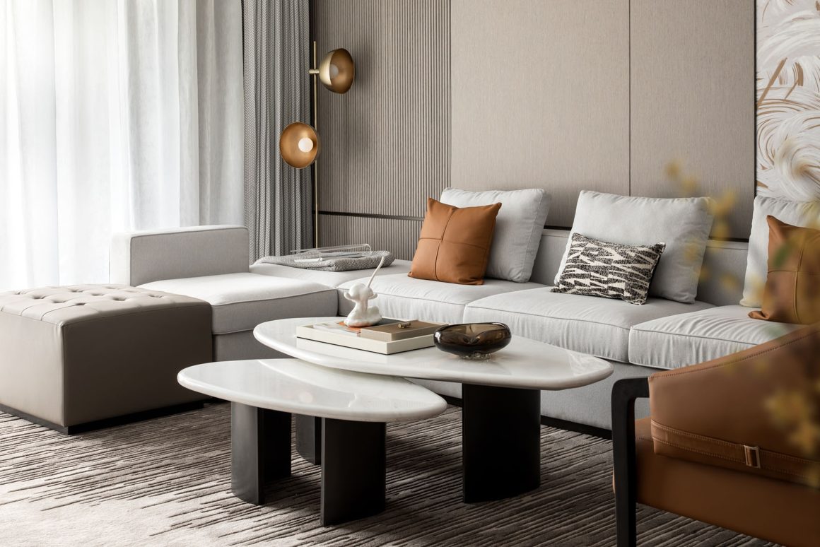 Salon moderne avec canapé beige, coussins marron, tables basses blanches, fauteuil et tapis texturé.
