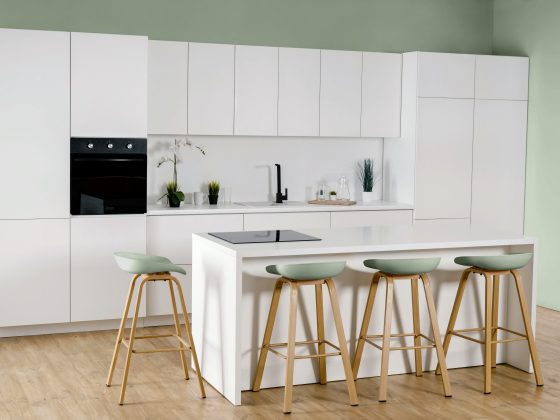 Tendance cuisine 2025 avec îlot central, tabourets bois et vert, mur vert clair, sol bois clair et design épuré.