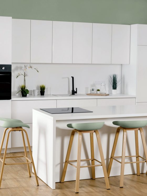 Tendance cuisine 2025 avec îlot central, tabourets bois et vert, mur vert clair, sol bois clair et design épuré.