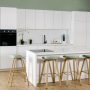 Tendance cuisine 2025 avec îlot central, tabourets bois et vert, mur vert clair, sol bois clair et design épuré.