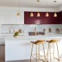 Style de cuisine moderne avec îlot blanc, meubles bordeaux, armoires blanches, accents dorés, électroménagers inox et luminaires suspendus.