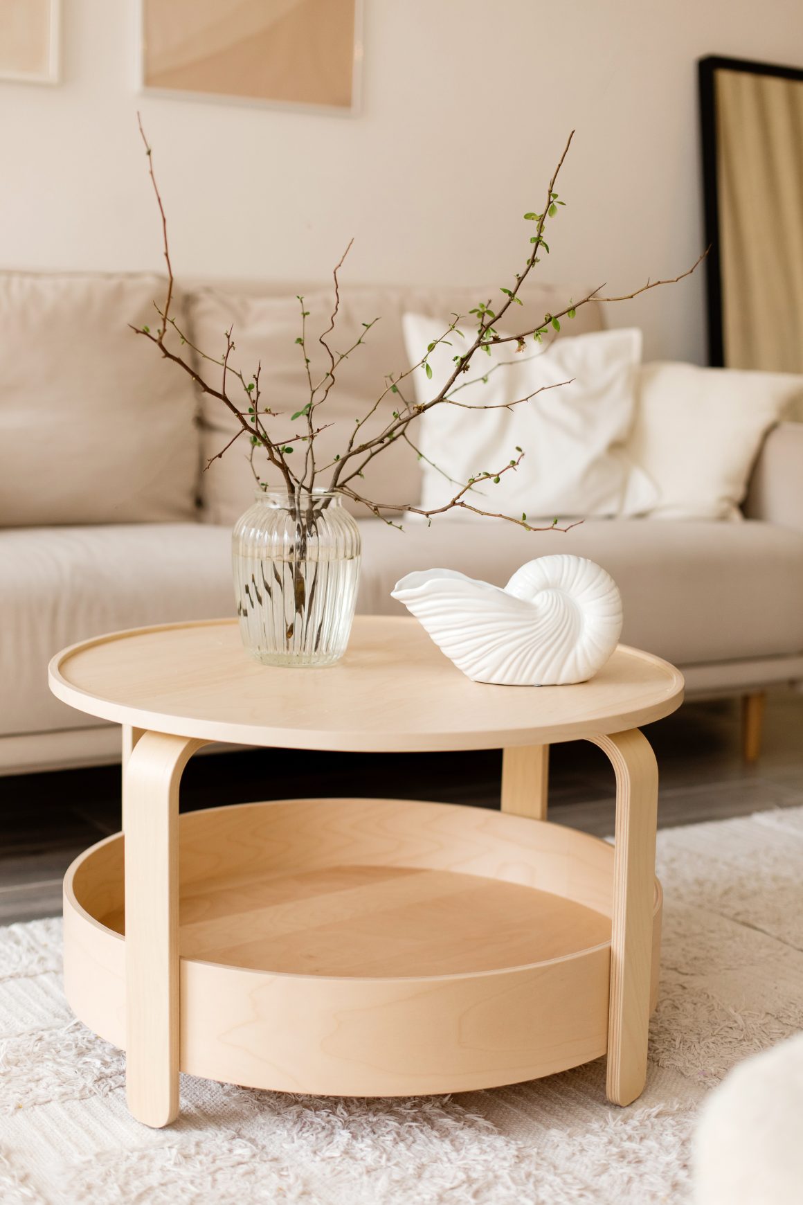 Déco salon avec table basse ronde en bois clair incluant vase transparent et coquillage blanc.