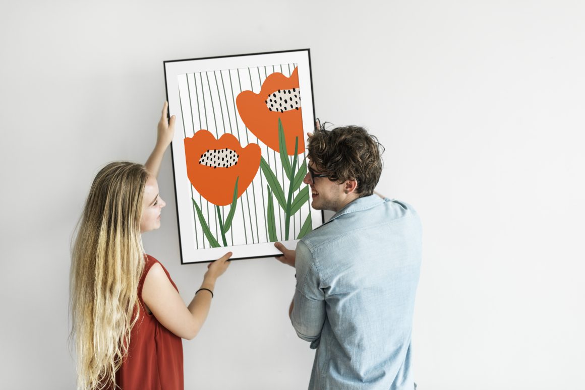 Deux personnes accrochent un tableau sans percer le mur.