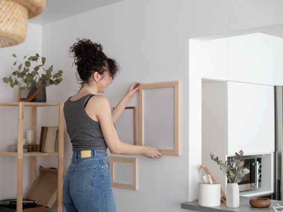 Une jeune femme est en train d'accrocher un tableau sans trou dans un intérieur minimaliste.