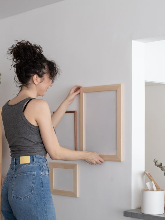 Une jeune femme est en train d'accrocher un tableau sans trou dans un intérieur minimaliste.