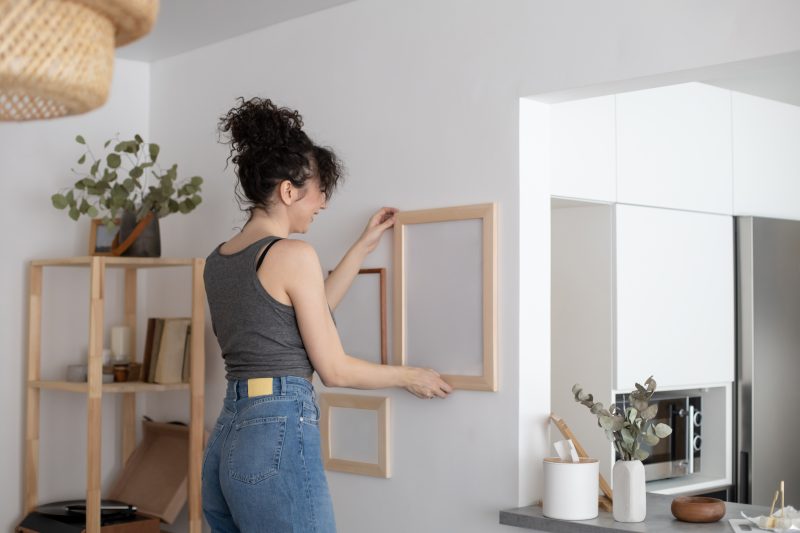 Une jeune femme est en train d'accrocher un tableau sans trou dans un intérieur minimaliste.