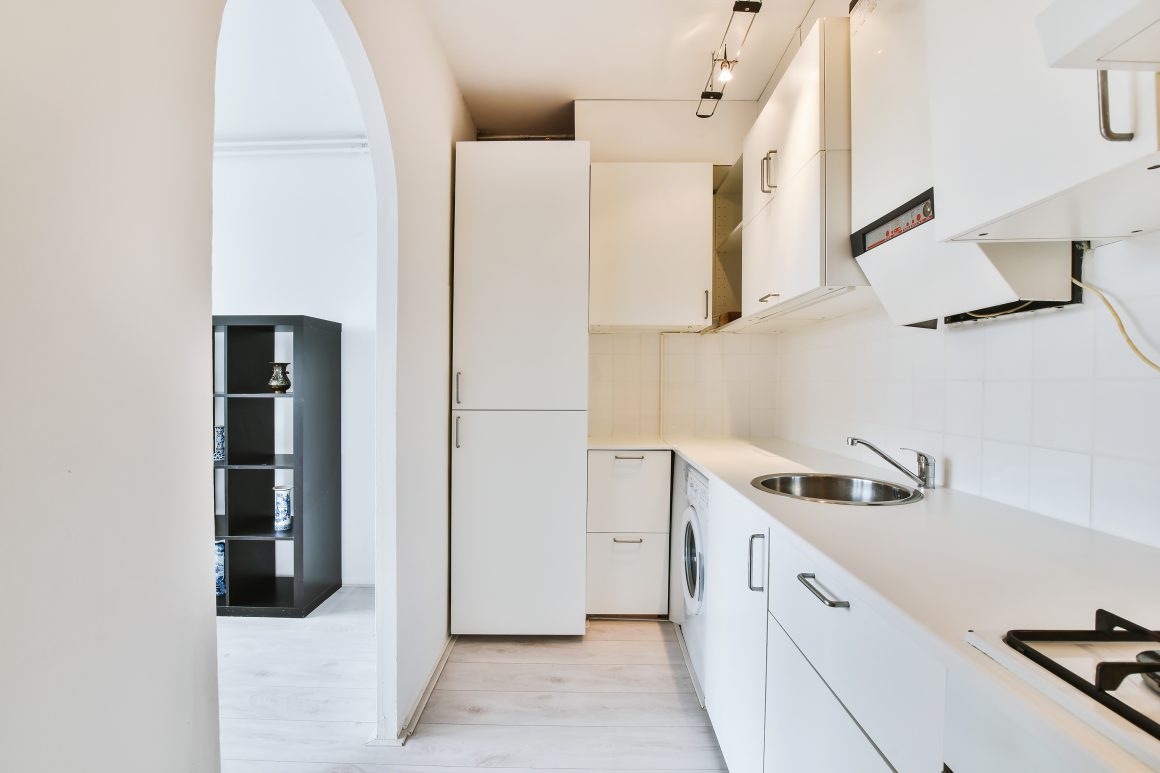 Aménagement cuisine 4m2 minimaliste avec armoire haute, machine à laver, petit évier et plan de travail épuré.