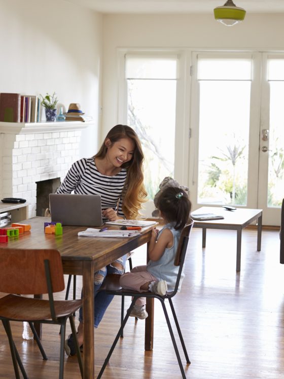 Une femme assise à une table avec une petite fille jouant, dans un salon lumineux et chaleureux.