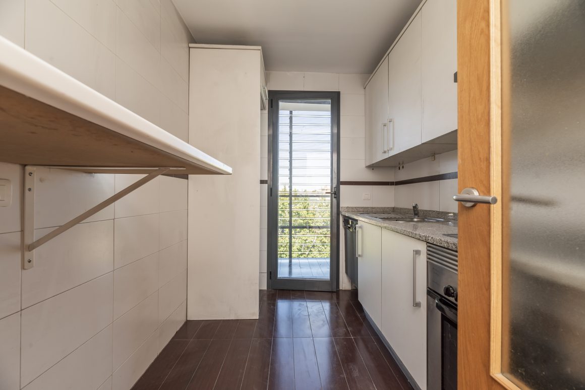 Cuisine étroite avec plan de travail en granit, placards blancs, plaque de cuisson, évier et four intégré.