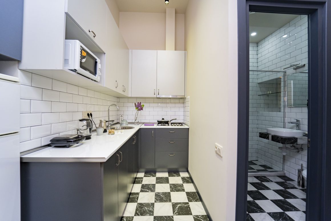Cuisine 4m2 fonctionnelle, avec des armoires grises et blanches, un carrelage à carreaux noir et blanc et un micro-ondes encastré.