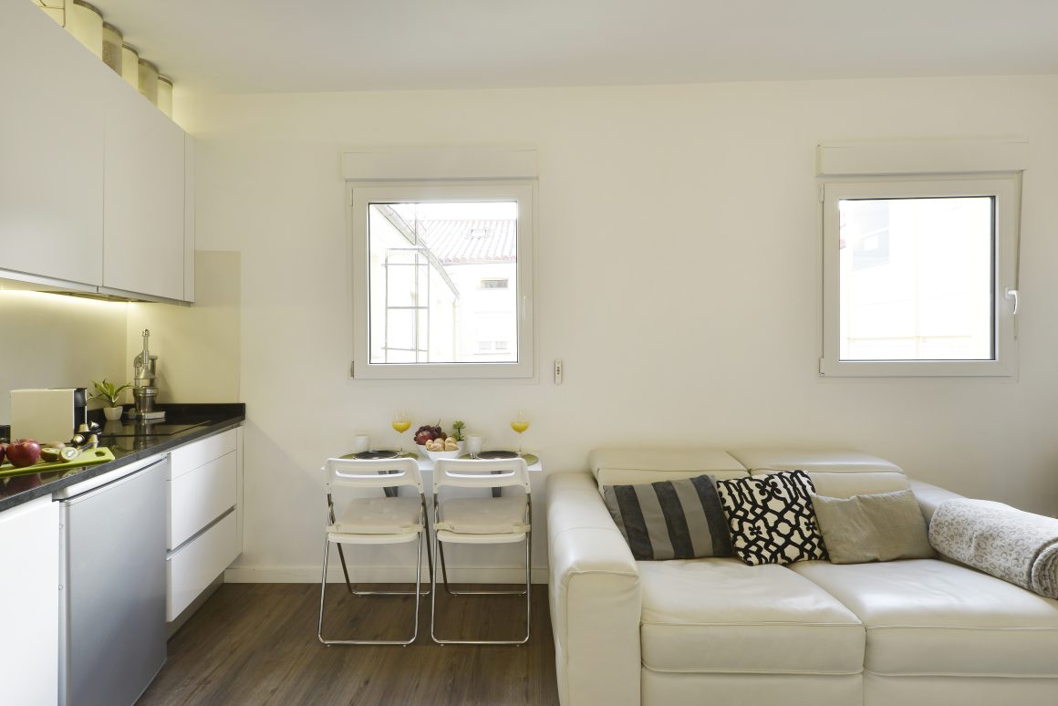 Cuisine compacte et moderne, coin repas simple avec deux chaises et salon avec canapé.