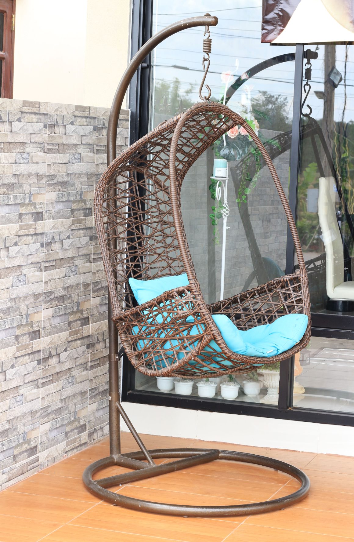 Chaise suspendue en osier brun avec coussins bleus pour aménager une petite terrasse.