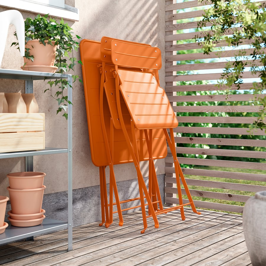 Petite terrasse aménagée avec chaises pliantes orange, pots de plantes et clôture en bois.