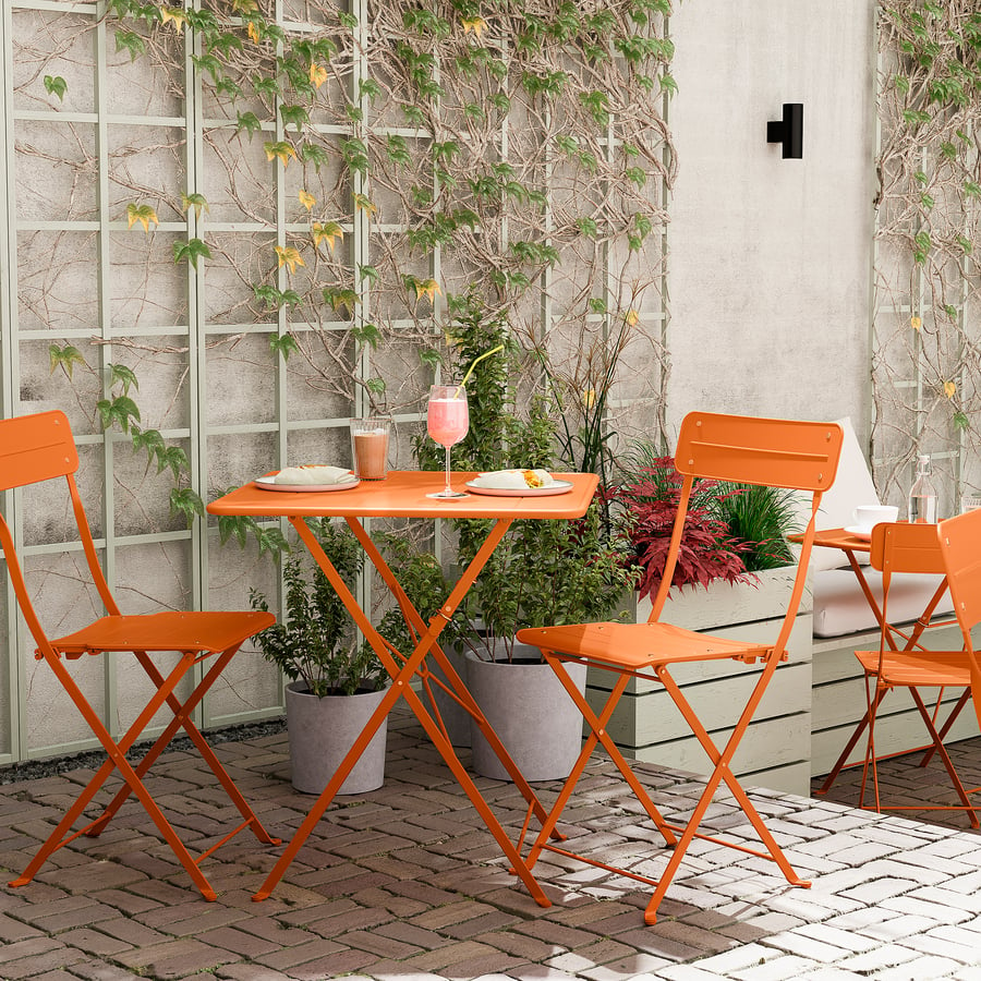 Terrasse cosy avec table orange, chaises , plantes vertes et mur en béton.
