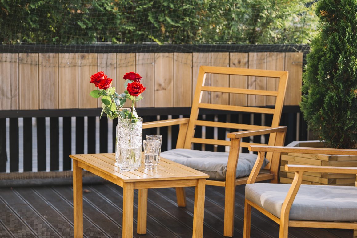 Terrasse avec chaises en bois et table basse incluant verre d'eau et vase avec trois roses rouges.