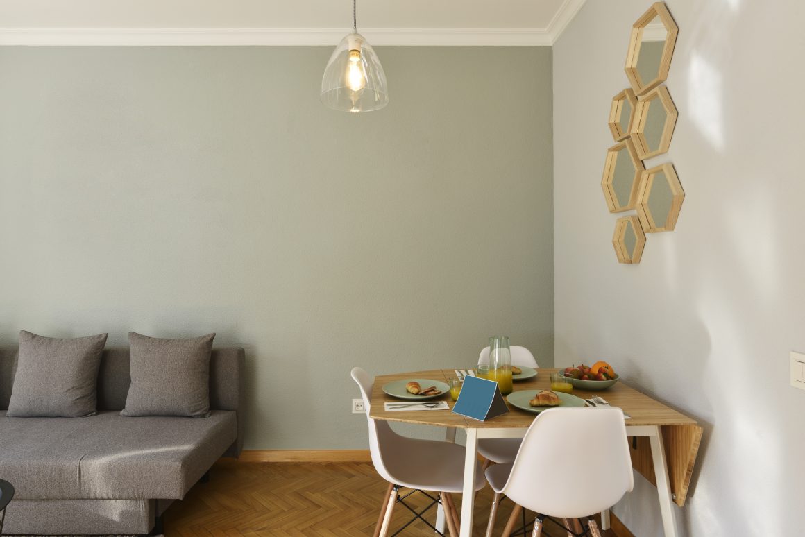 Salon salle à manger dans 20m2 aménagés avec canapé, table en bois, chaises, miroirs et suspension.