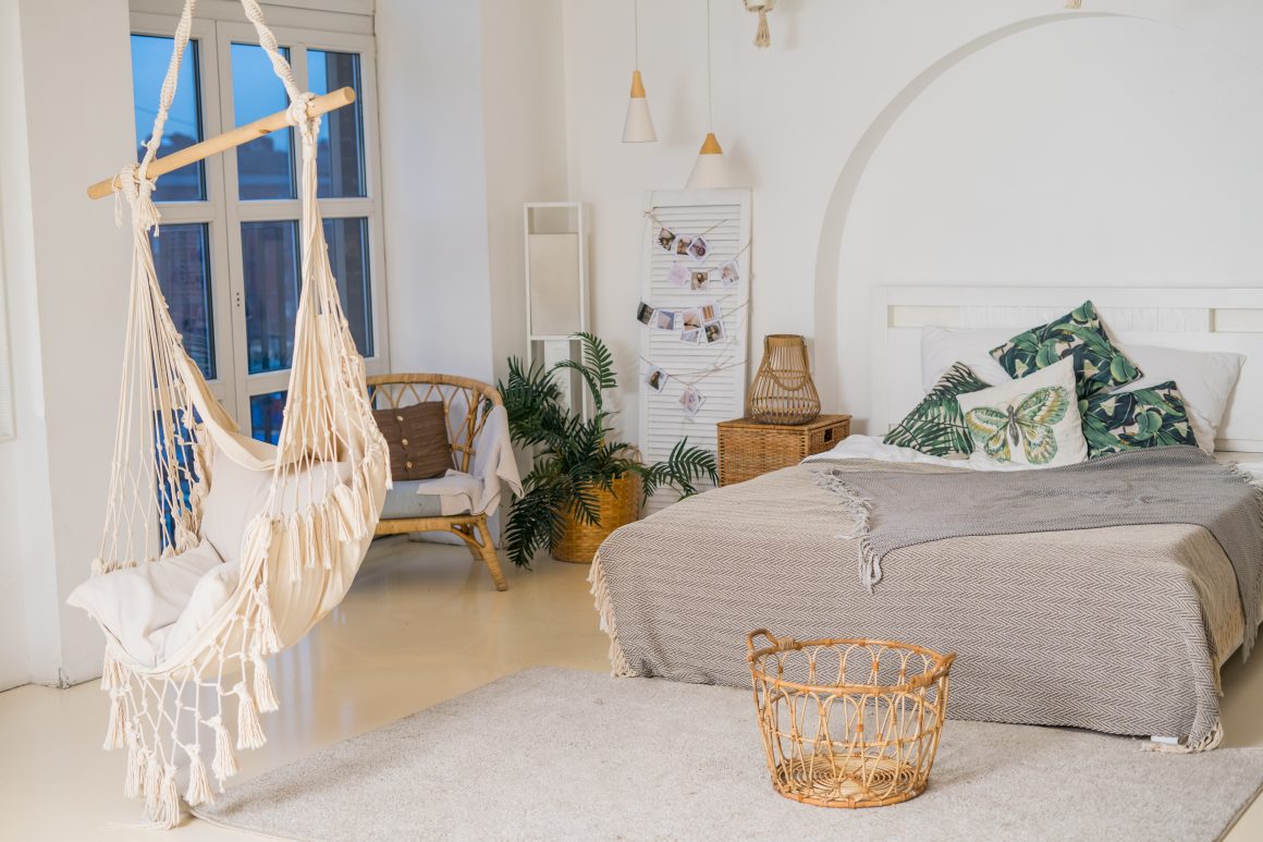 Déco chambre bohème avec hamac en macramé, coussins verts à motifs, fauteuil en rotin et plante.