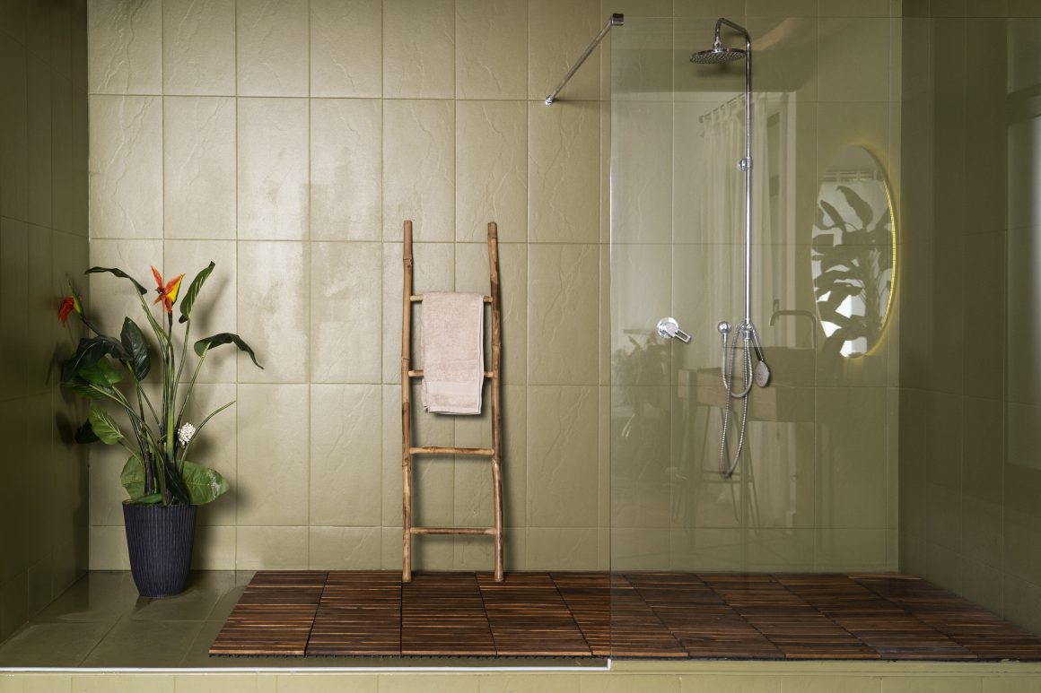 Salle de bain avec carrelage vert, douche à l’italienne, échelle porte-serviette et plante décorative.