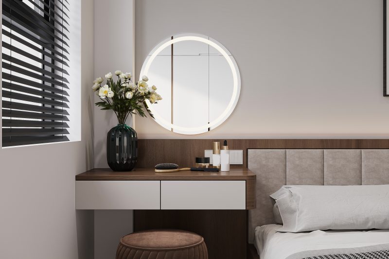 Un coin chambre moderne avec coiffeuse en bois, miroir rond lumineux, tabouret marron, fleurs blanches, et coussin gris clair.