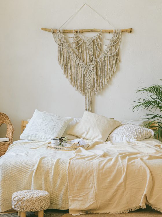 Chambre style bohème avec murs clairs, literie crème, fauteuil en osier, plante verte et tapis beige.
