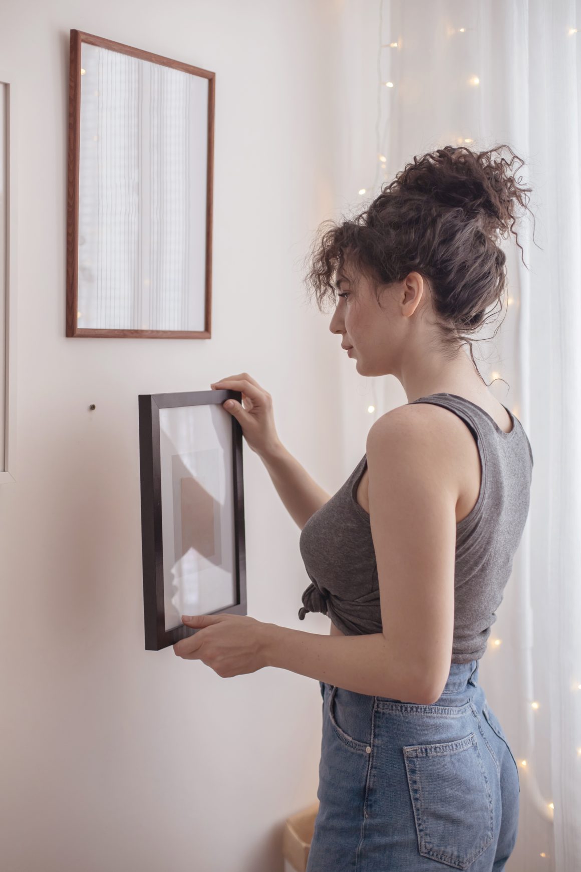 Femme accrochant cadre photo, dans un mur blanc.