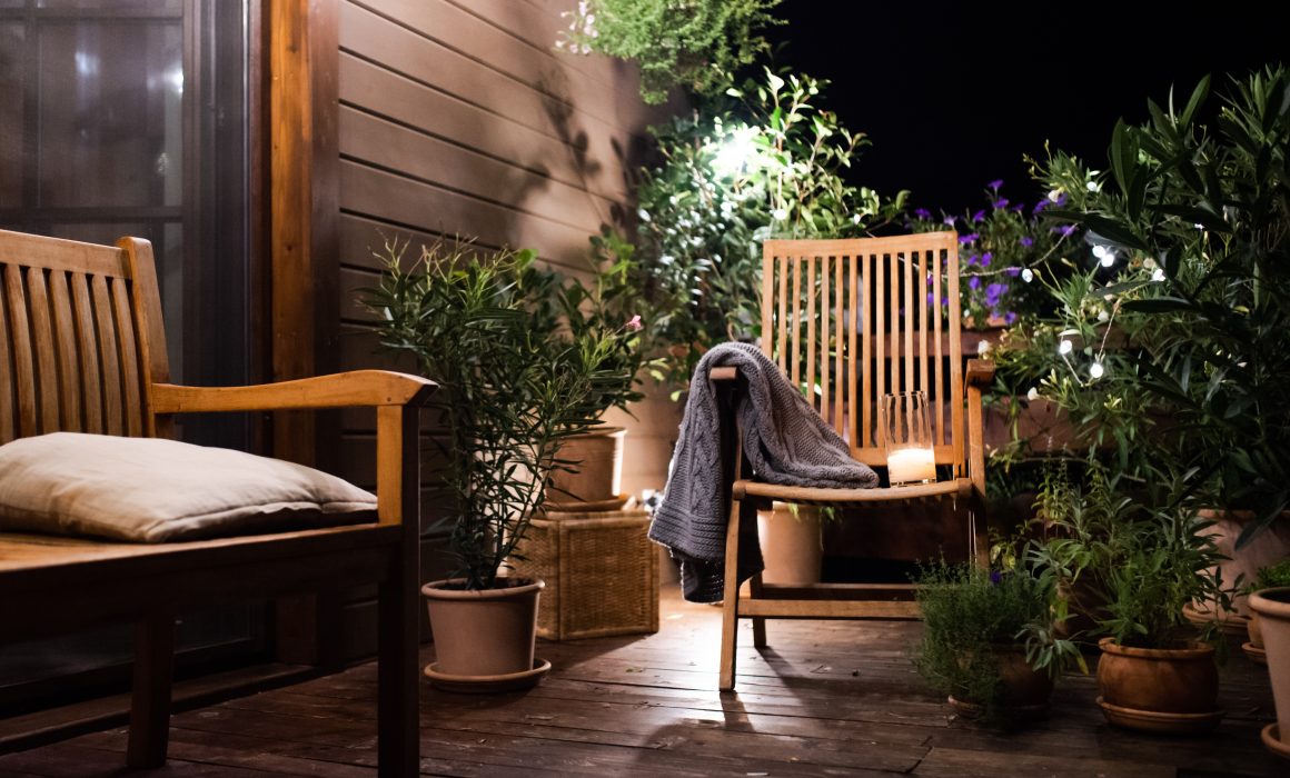 Terrasse cosy avec mobilier en bois, plantes vertes et guirlandes lumineuses.