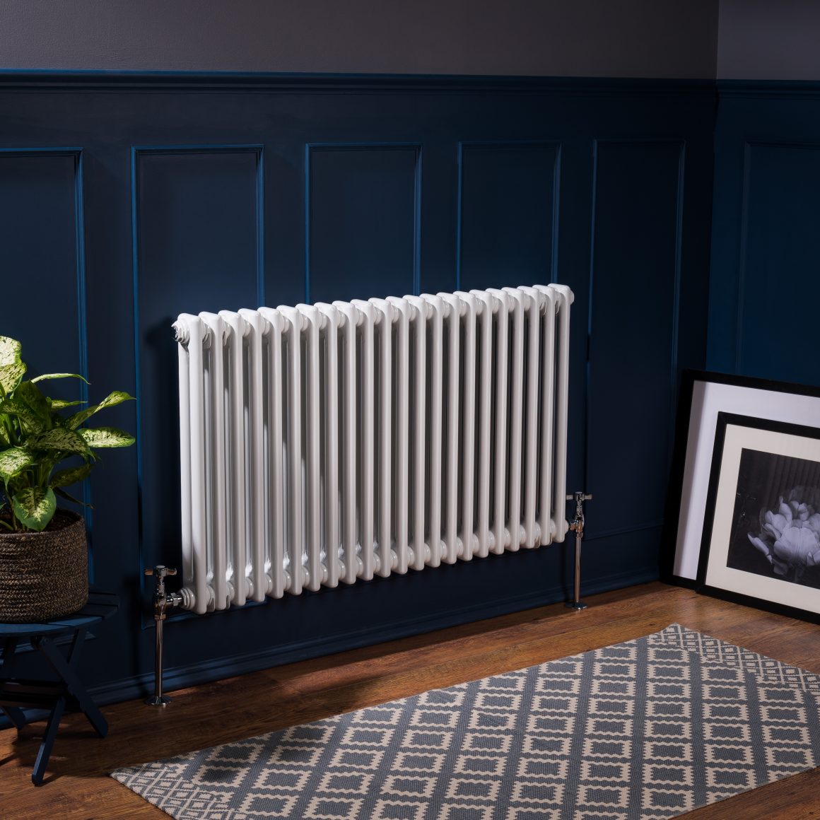 Radiateur électrique fixé à un mur bleu dans un petit espace incluant tapis, plante et une œuvre d'art.