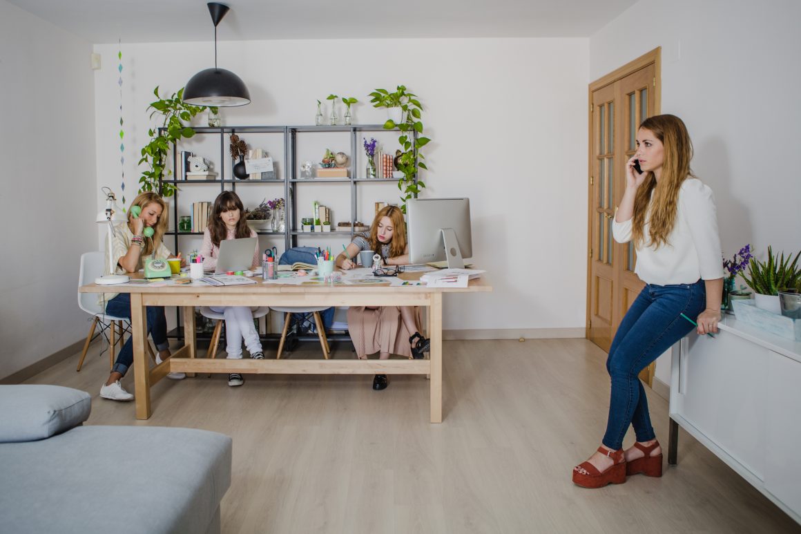 Quatre femmes travaillent dans un espace ouvert lumineux, entourées d'ordinateurs, papiers, plantes et déco moderne.
