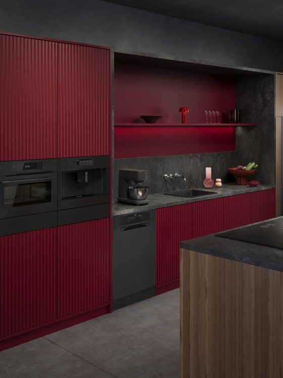modèle de cuisine moderne aux tons bordeaux et gris avec appareils encastrés noirs, plan de travail en pierre et îlot en bois.