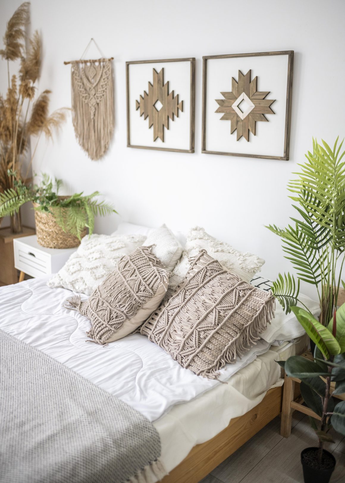 Décoration chambre bohème avec deux cadres en bois avec motifs géométriques, un macramé suspendu et plantes vertes.
