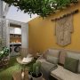 Petite terrasse aménagée avec canapé, fauteuil, plantes variées, tapis gazon et déco murale macramé.
