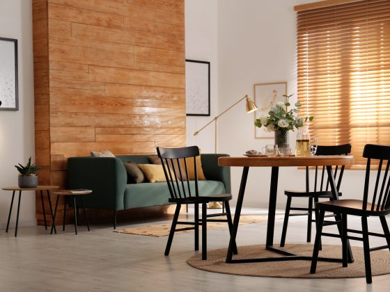 Aménager salon salle à manger 20m2 avec canapé vert, tables basses, table à manger avec chaises noires, tapis et stores en bois.