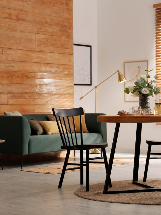 Aménager salon salle à manger 20m2 avec canapé vert, tables basses, table à manger avec chaises noires, tapis et stores en bois.