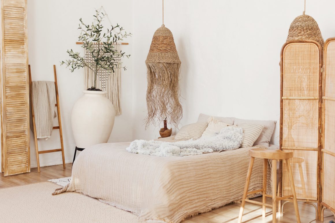 Chambre bohème aux tons beige naturel incluant lit avec plaid moelleux, vases et lampe suspendue en fibres naturelles.