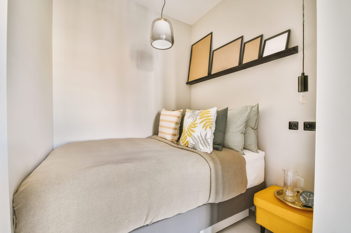 Petit coin nuit cosy avec lit, étagère murale avec cadres, suspension et table d'appoint jaune.