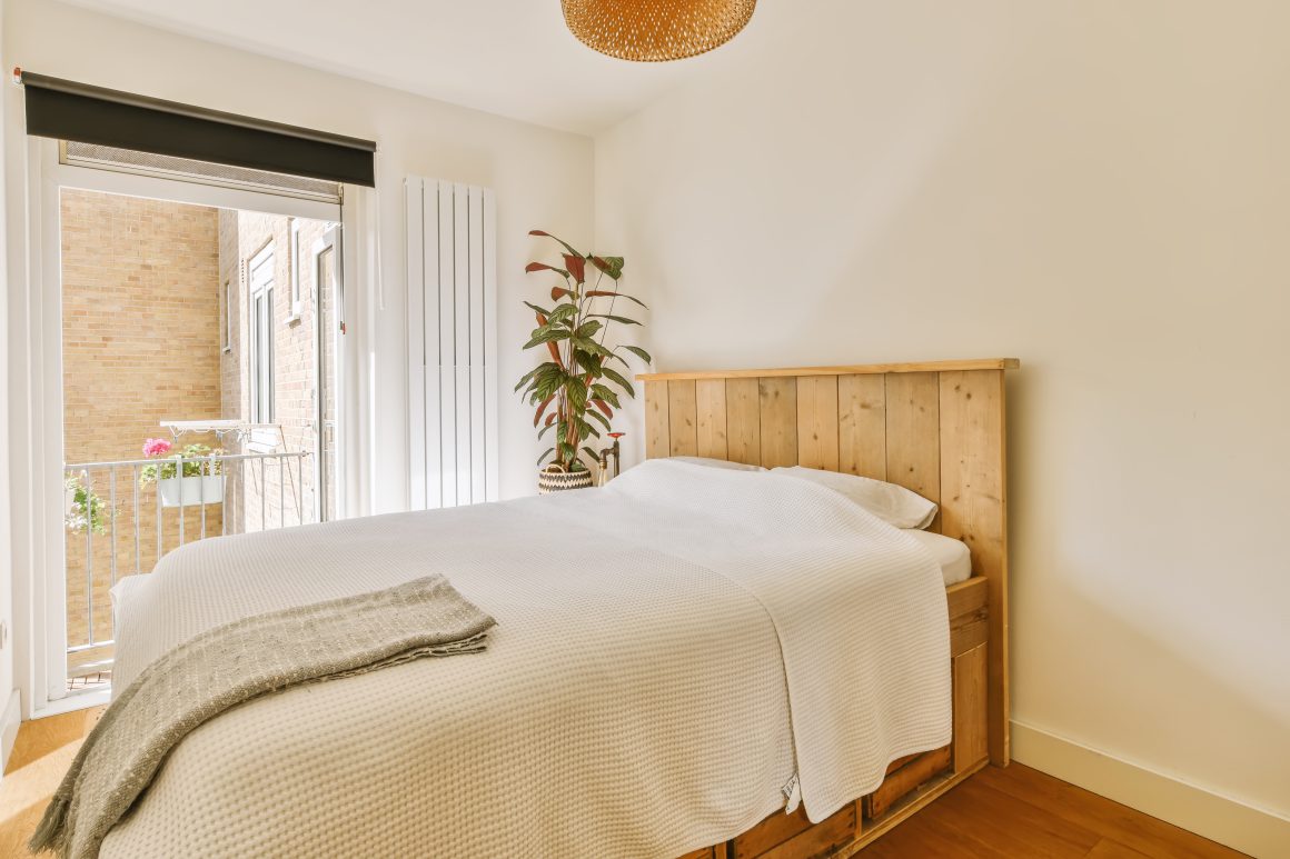 Chambre lumineuse et minimaliste avec lit en bois, plante d’angle et un petit balcon