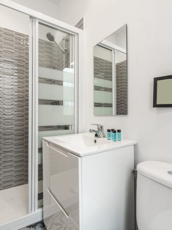 Aménagement petite salle de bain avec cabine douche vitrée, lavabo avec meuble blanc, miroir et toilettes.