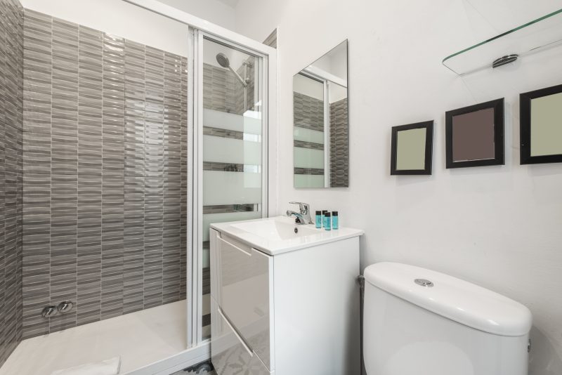 Aménagement petite salle de bain avec cabine douche vitrée, lavabo avec meuble blanc, miroir et toilettes.