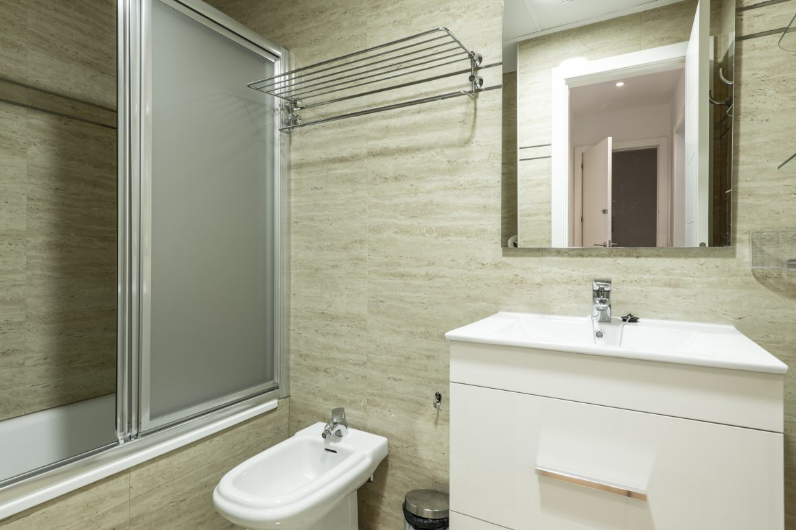 Aménagement petite salle de bain 4m2 avec lavabo blanc, miroir, bidet et baignoire avec paroi coulissante.