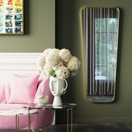 Salon élégant avec canapé rose, bouquet blanc dans vase sculptural et un mur vert incluant miroir doré.
