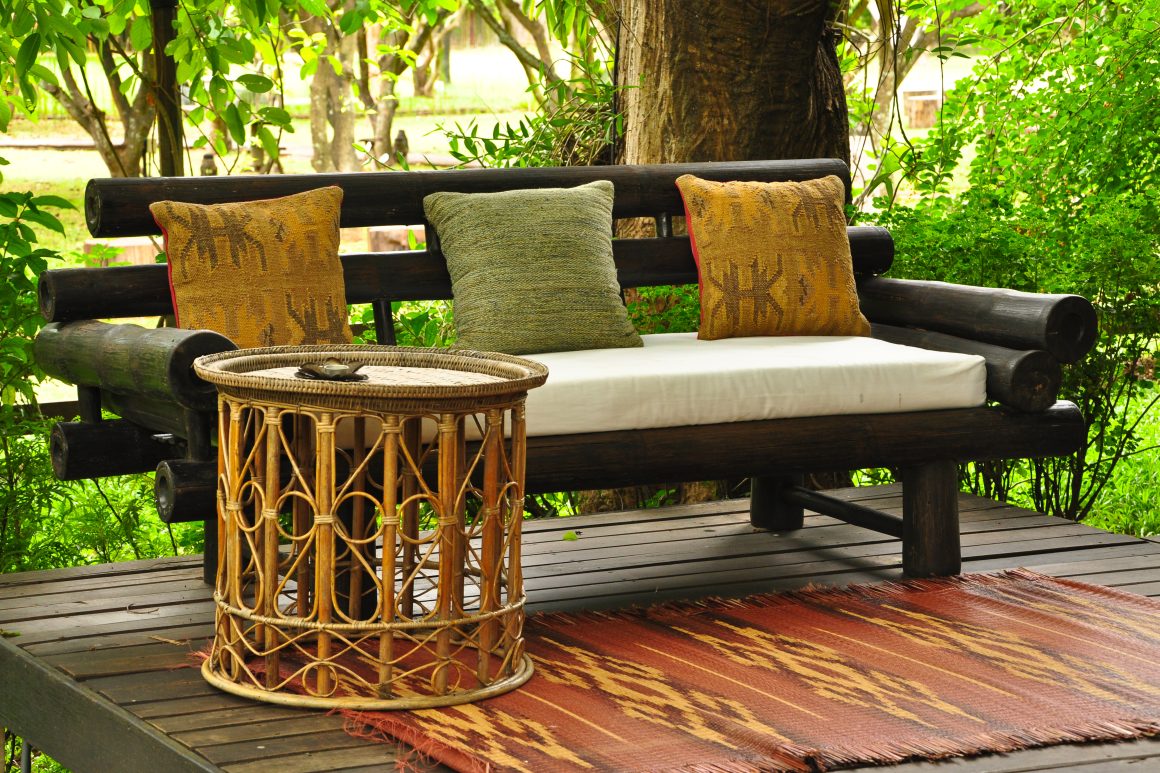 Coin salon de jardin aménagé avec un banc en bois foncé, table en osier ronde et tapis.