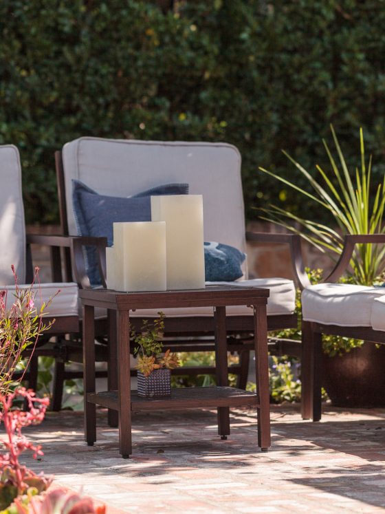 Aménager un coin salon de jardin avec des fauteuils rembourrés et une petite table en bois avec bougies,