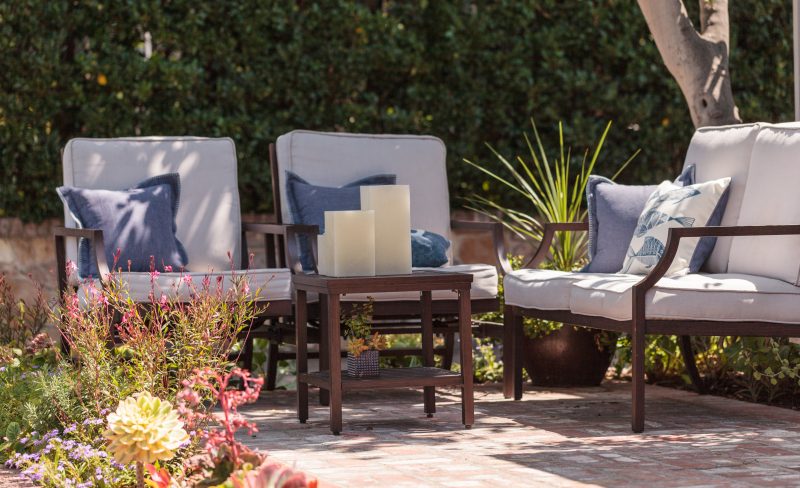 Aménager un coin salon de jardin avec des fauteuils rembourrés et une petite table en bois avec bougies,