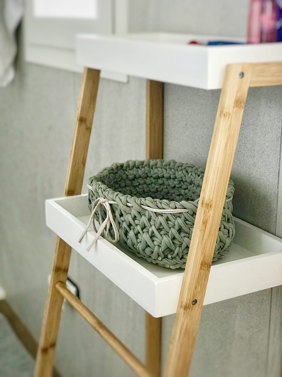 Panier vert tricoté posé sur une étagère blanche pour ranger serviettes salle de bain