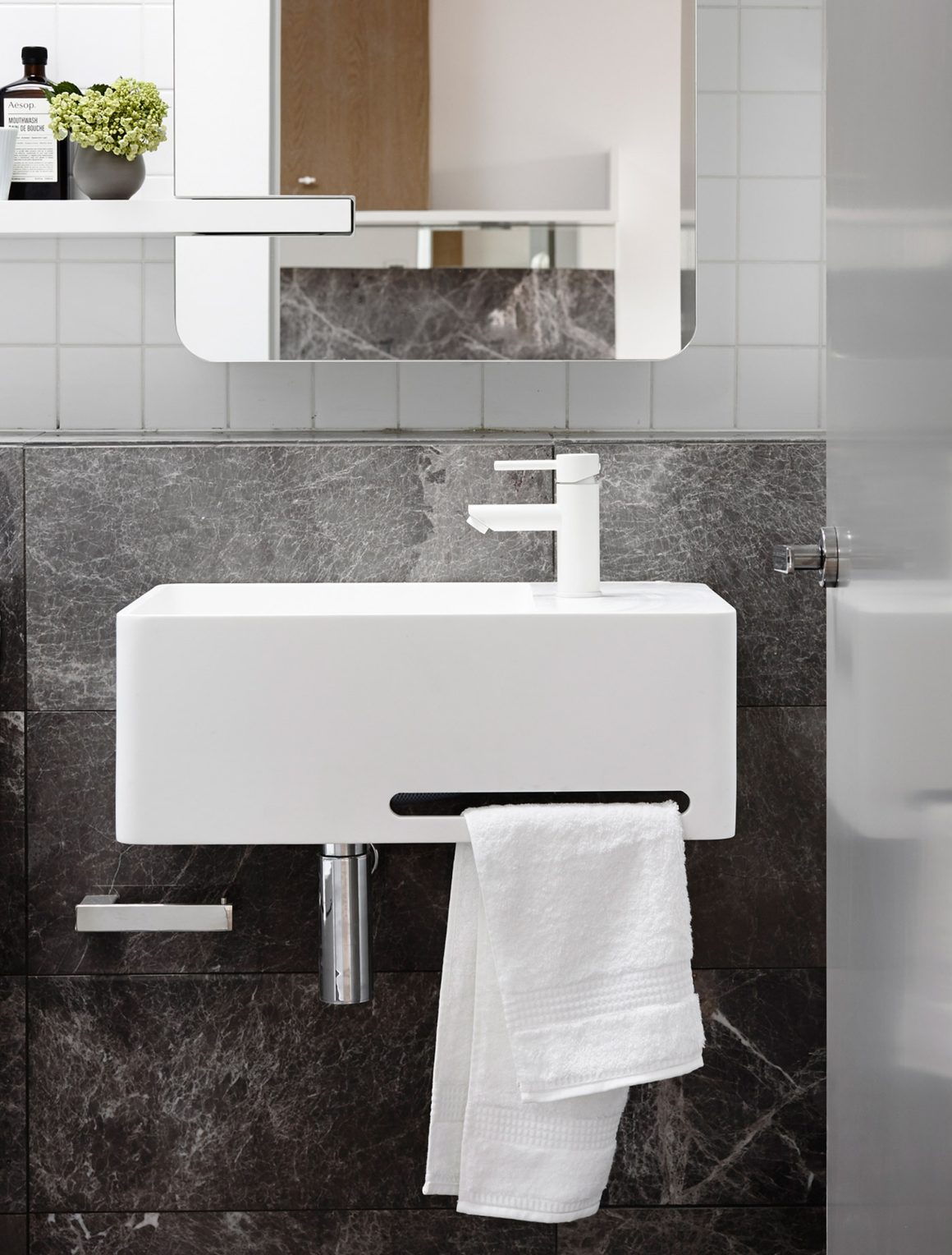 Meuble lave mains avec robinet assorti, serviette suspendue, mur en carrelage gris foncé et miroir.