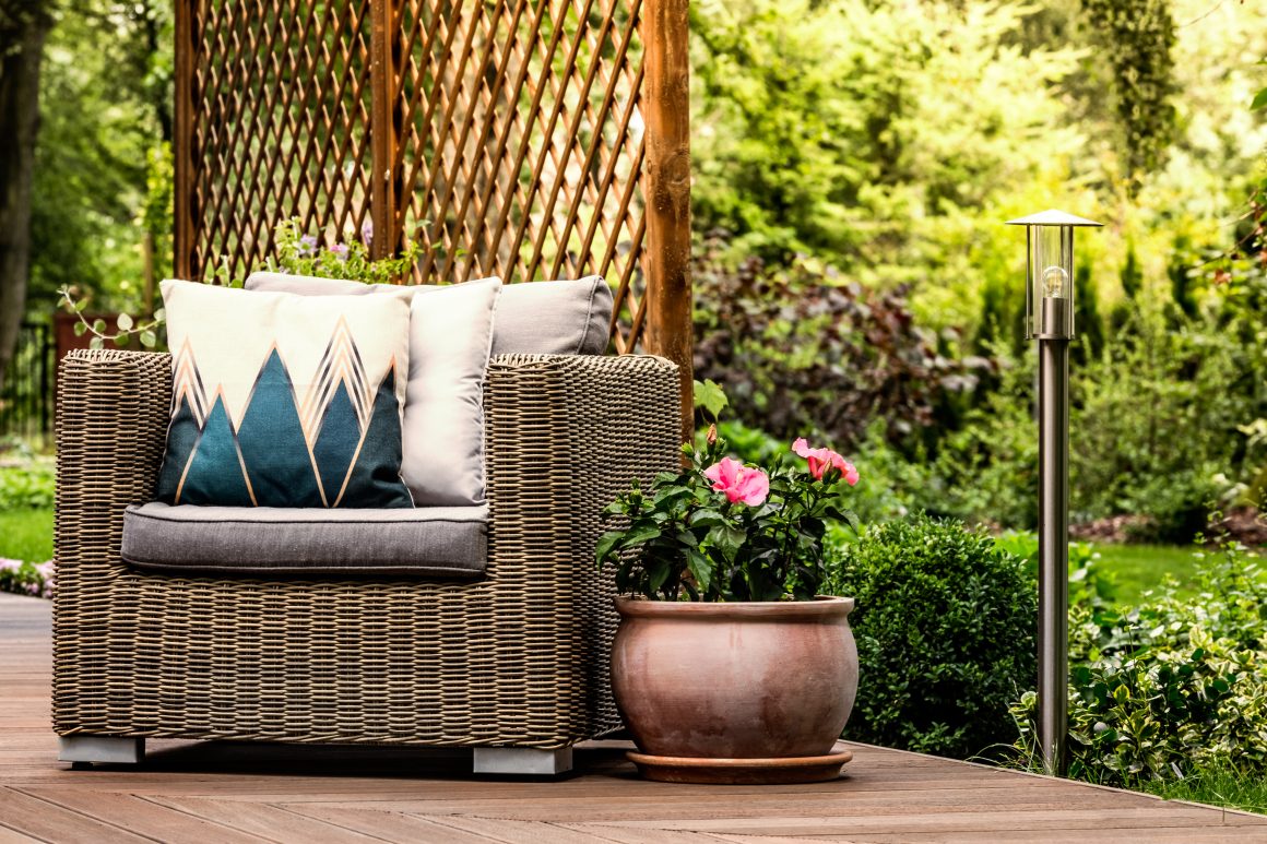 Fauteuil en rotin cosy sur terrasse en bois avec coussins décoratifs et pot de fleurs roses