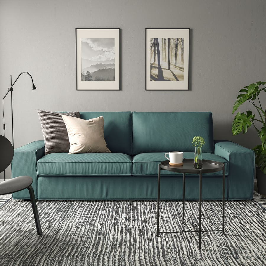 Canapé bleu, table ronde, tapis rayé, deux cadres photo, plante avec mur gris dans un intérieur zen.