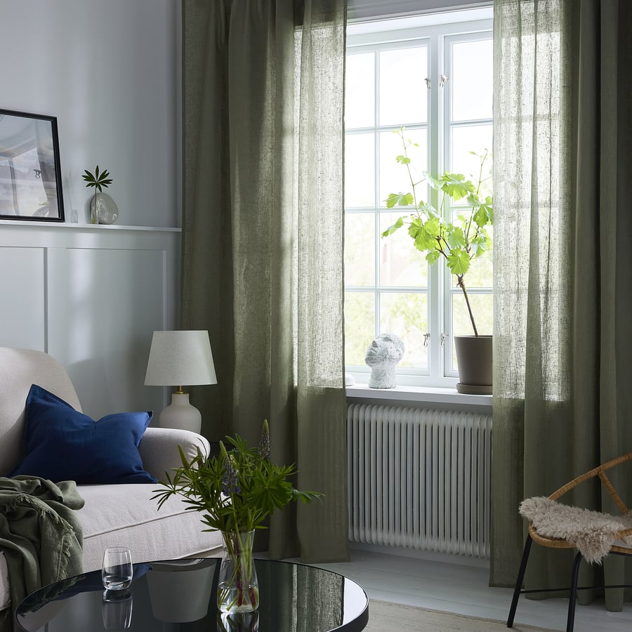 Salon zen et lumineux avec canapé beige, coussin bleu, rideaux verts, plante et chaise en osier.
