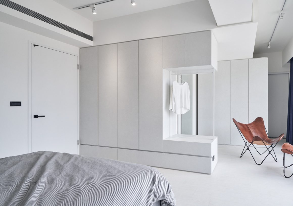 Chambre incluant grande armoire intégrée, fauteuils en cuir marron, lit et éclairage discret